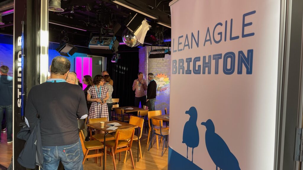 Photo from a previous Lean Agile Brighton, one of the three Lean Agile events you really shouldn't miss. A Lean Agile Brighton banner is on the right, with people milling in the background on the left.